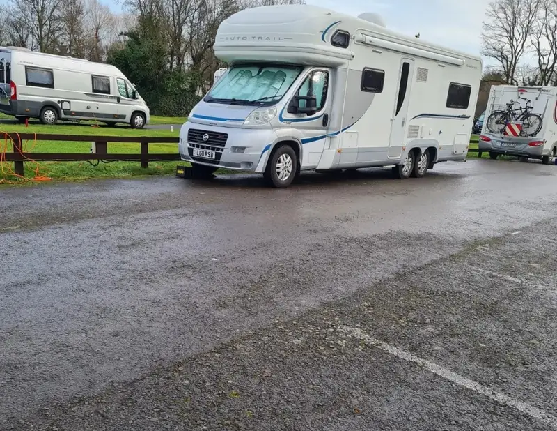 Large white Fiat motorhome parked on a wet tarmac site with bare trees behind (recent job)